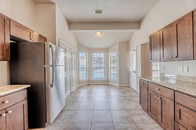 kitchen featuring light stone countertops, stainless steel fridge, lofted ceiling with beams, and a textured ceiling