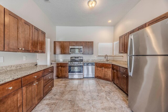 kitchen with sink, light stone countertops, a textured ceiling, and appliances with stainless steel finishes