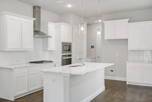 kitchen featuring wall chimney exhaust hood, stainless steel appliances, an island with sink, and sink