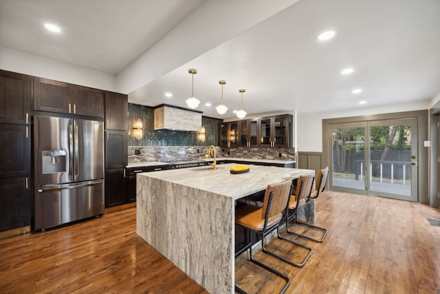 kitchen with stainless steel appliances, backsplash, a center island with sink, hardwood / wood-style floors, and decorative light fixtures