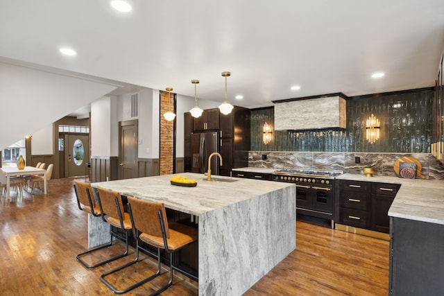 kitchen with appliances with stainless steel finishes, light wood-type flooring, sink, pendant lighting, and light stone counters