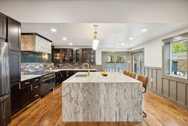 kitchen with a kitchen island with sink, stainless steel appliances, a healthy amount of sunlight, sink, and light wood-type flooring