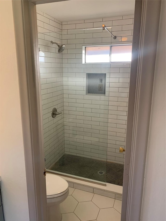 bathroom featuring tile patterned flooring, a tile shower, and toilet