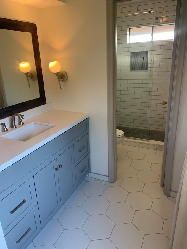 bathroom with a tile shower, vanity, tile patterned flooring, and toilet