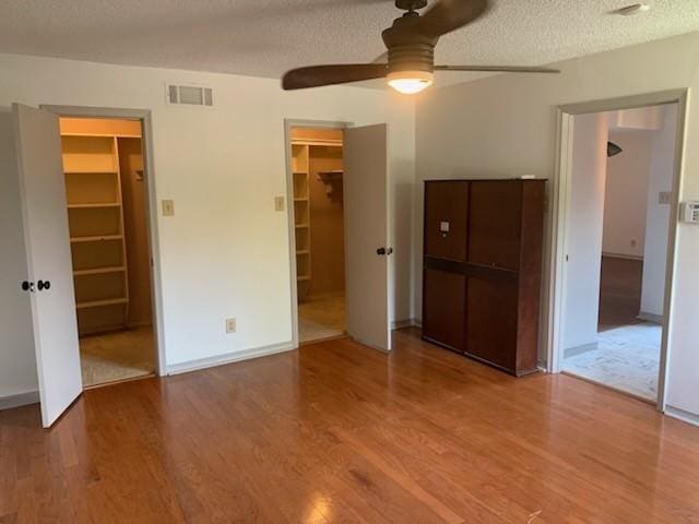 unfurnished bedroom featuring a walk in closet, a textured ceiling, ceiling fan, and a closet