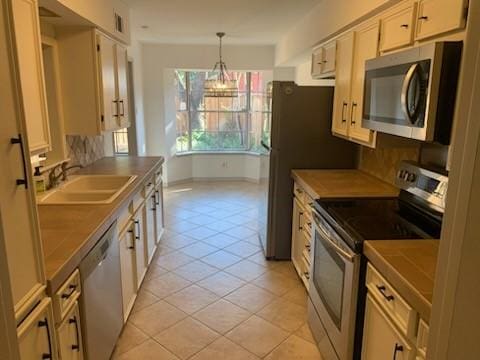 kitchen featuring sink, tile countertops, light tile patterned floors, pendant lighting, and stainless steel appliances