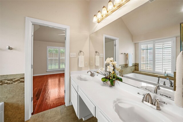 bathroom with double vanity, wood-type flooring, vaulted ceiling, and a bathing tub