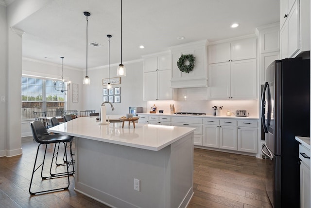 kitchen with stainless steel refrigerator, white cabinets, a kitchen breakfast bar, hanging light fixtures, and a kitchen island with sink