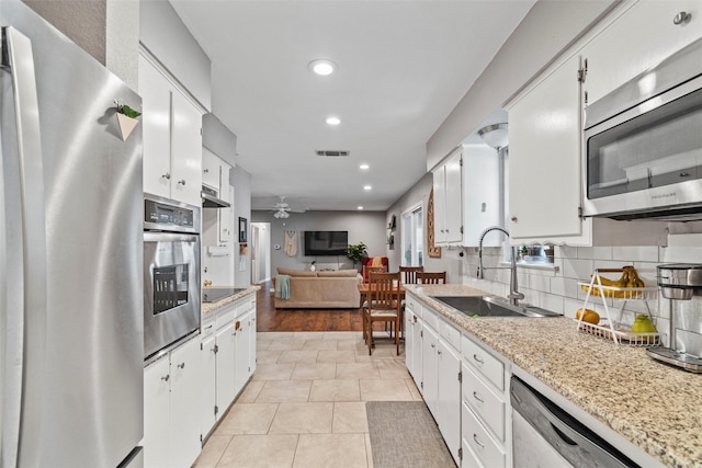 kitchen with light wood-type flooring, white cabinets, backsplash, appliances with stainless steel finishes, and sink