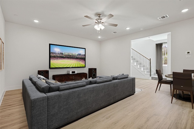 living room with a ceiling fan, visible vents, stairway, and light wood-style flooring