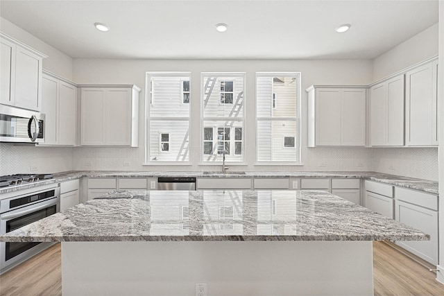 kitchen with light stone counters, stainless steel appliances, backsplash, a sink, and light wood-type flooring