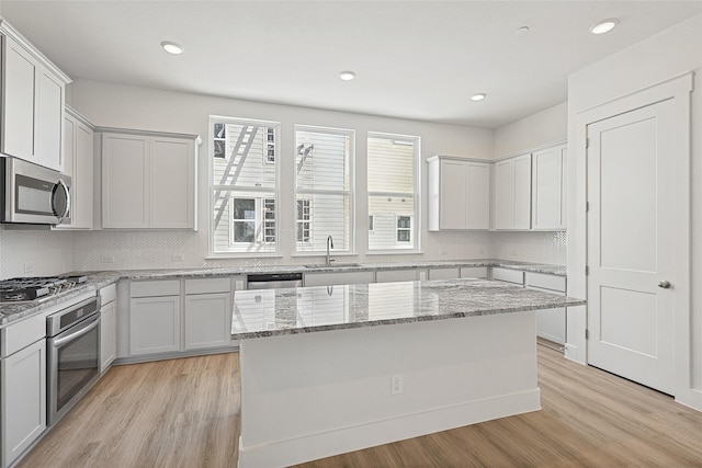 kitchen featuring light wood-style floors, stainless steel appliances, backsplash, and a sink