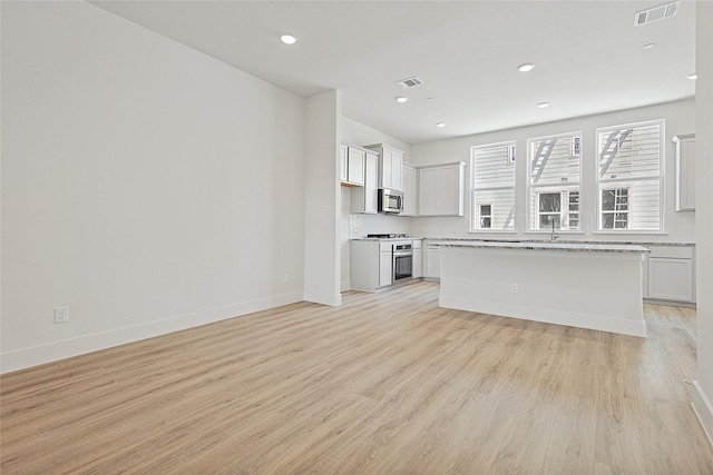 unfurnished living room with light wood finished floors, visible vents, and baseboards