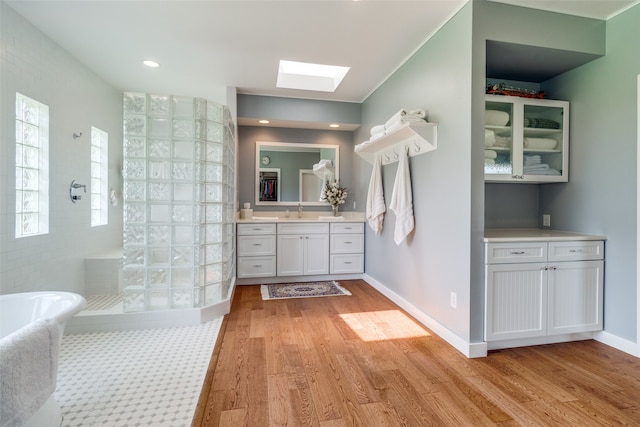 bathroom with plus walk in shower, hardwood / wood-style floors, vanity, and a skylight