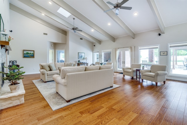 living room featuring a skylight, ceiling fan, beamed ceiling, high vaulted ceiling, and light hardwood / wood-style floors