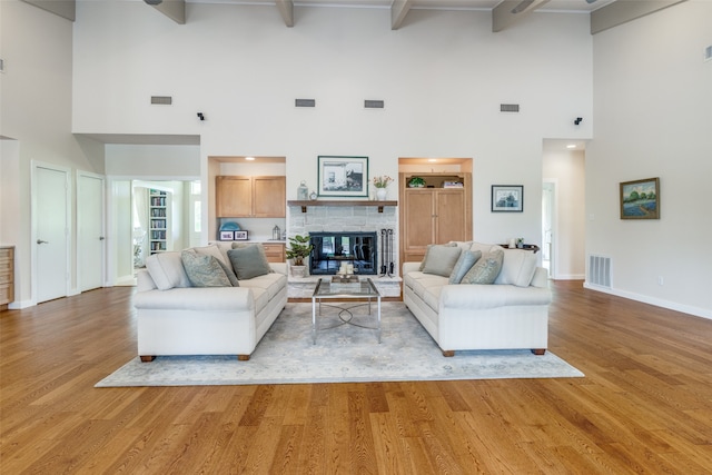 living room with a fireplace, a high ceiling, light hardwood / wood-style floors, and beam ceiling