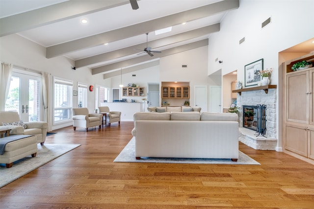 living room with ceiling fan, french doors, a stone fireplace, high vaulted ceiling, and light wood-type flooring