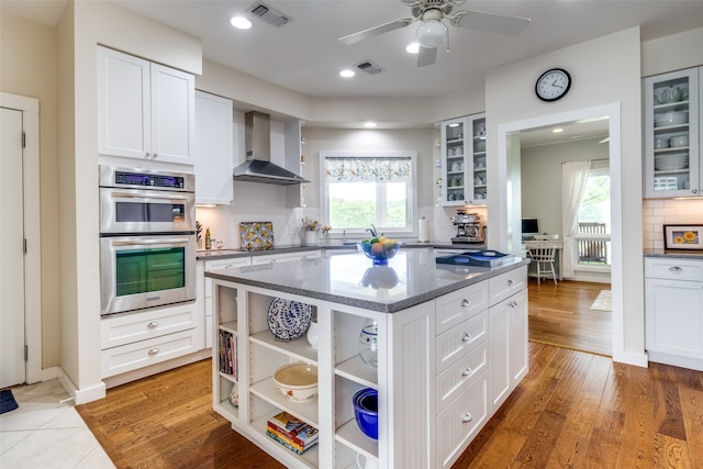 kitchen featuring white cabinets, a center island, wall chimney range hood, and tasteful backsplash