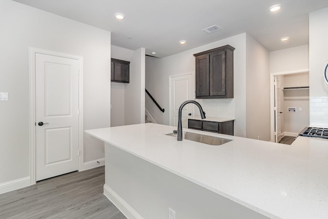 kitchen with dark brown cabinetry, sink, light hardwood / wood-style flooring, and kitchen peninsula