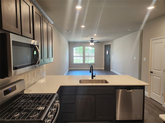 kitchen featuring dark wood-type flooring, sink, kitchen peninsula, stainless steel appliances, and backsplash