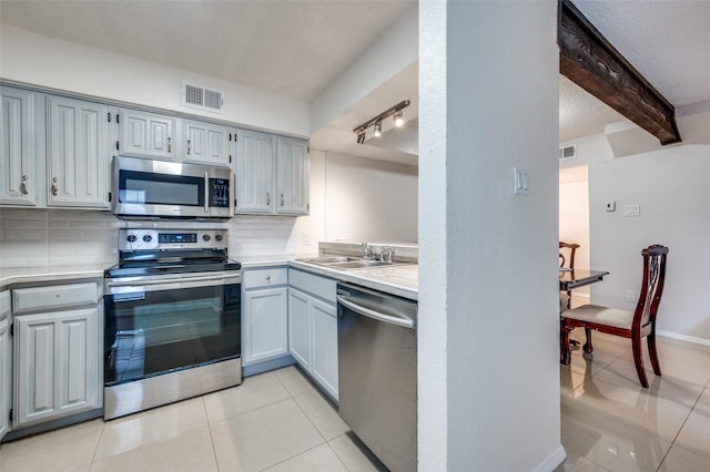 kitchen featuring appliances with stainless steel finishes, beamed ceiling, sink, decorative backsplash, and light tile patterned floors