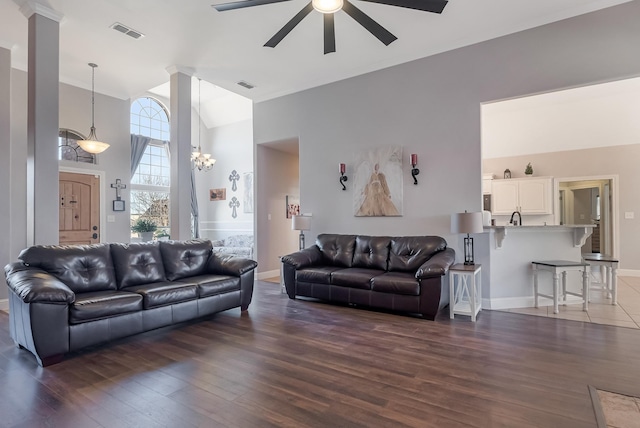 living room featuring dark hardwood / wood-style flooring, ceiling fan with notable chandelier, vaulted ceiling, and ornate columns