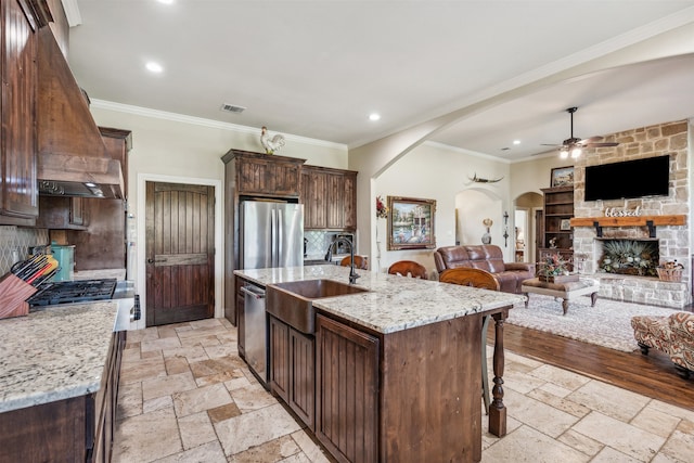 kitchen with light stone countertops, sink, backsplash, a center island with sink, and appliances with stainless steel finishes