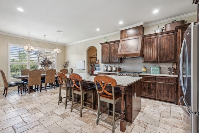 kitchen featuring stainless steel refrigerator, light stone countertops, a breakfast bar, a chandelier, and a center island with sink