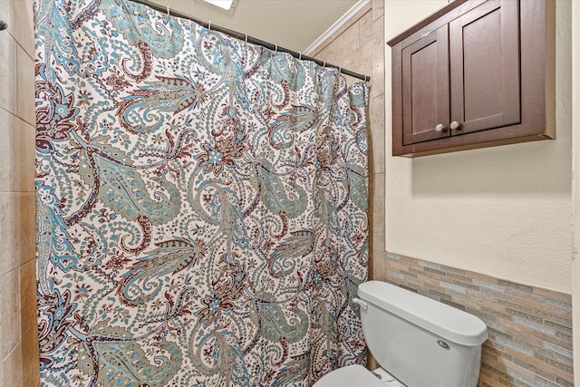 bathroom featuring toilet, a shower with shower curtain, and tile walls