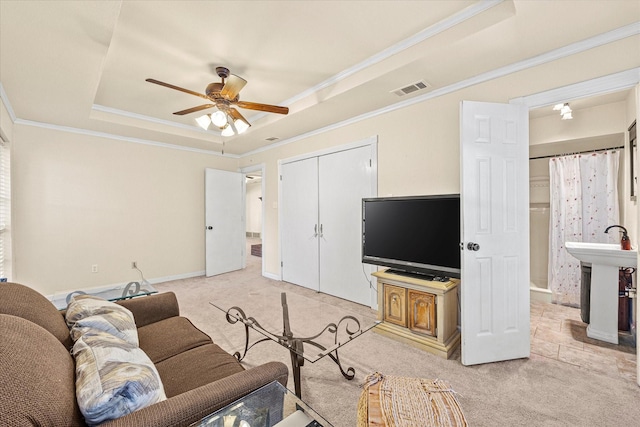 living room featuring a raised ceiling, ornamental molding, light carpet, and ceiling fan