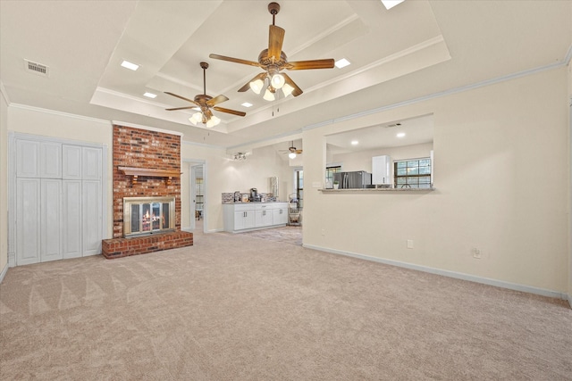 unfurnished living room with crown molding, light colored carpet, a tray ceiling, and a brick fireplace