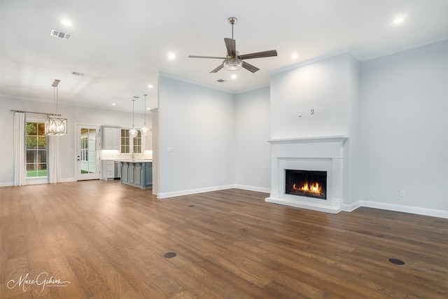 unfurnished living room with dark wood-type flooring, ceiling fan with notable chandelier, and ornamental molding