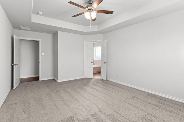 unfurnished bedroom with a tray ceiling, ceiling fan, ensuite bathroom, and light colored carpet