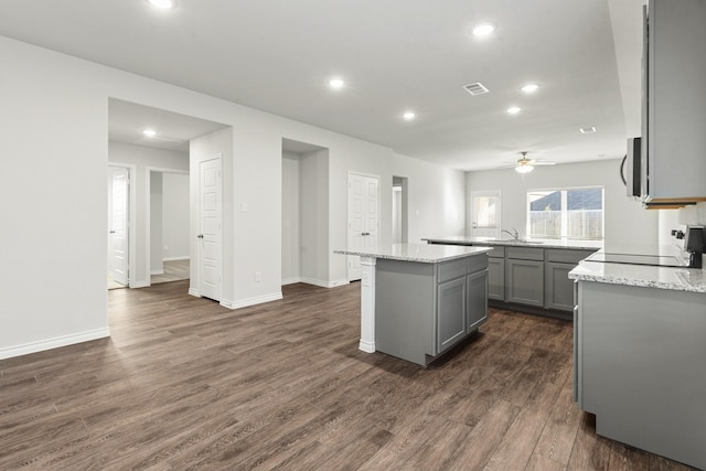 kitchen featuring dark hardwood / wood-style flooring, light stone counters, a center island, and gray cabinets