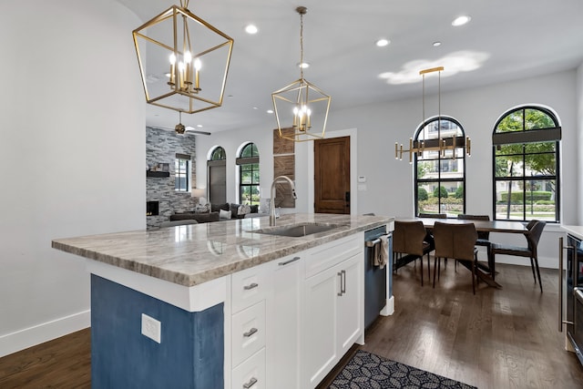 kitchen with dark wood-type flooring, light stone counters, an island with sink, decorative light fixtures, and sink