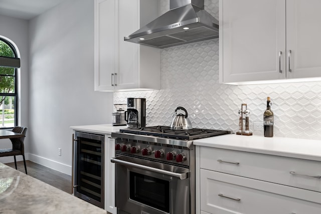 kitchen featuring high end range, wall chimney range hood, wine cooler, and white cabinetry