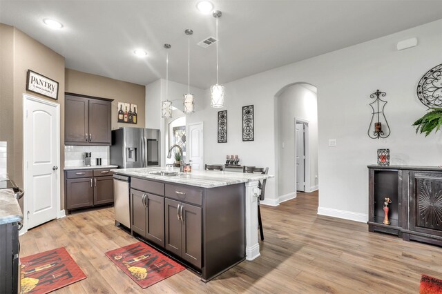 kitchen with hanging light fixtures, sink, light stone counters, light hardwood / wood-style floors, and appliances with stainless steel finishes