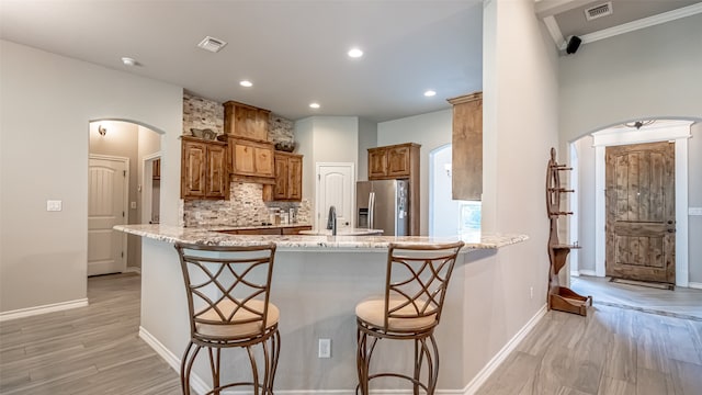 kitchen with a kitchen bar, kitchen peninsula, light wood-type flooring, light stone countertops, and stainless steel fridge with ice dispenser