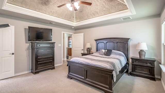 bedroom with a raised ceiling, light colored carpet, and ceiling fan