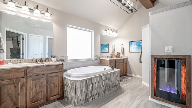 bathroom with vaulted ceiling with beams, vanity, hardwood / wood-style floors, and tiled bath