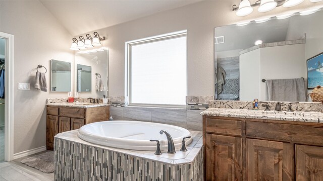 bathroom featuring a relaxing tiled tub, vanity, and lofted ceiling