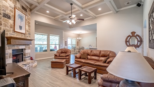 living room featuring a stone fireplace, light hardwood / wood-style floors, ceiling fan with notable chandelier, beam ceiling, and coffered ceiling