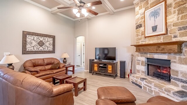 living room featuring a fireplace, light wood-type flooring, beam ceiling, ceiling fan, and ornamental molding