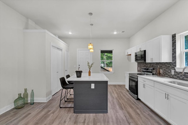 kitchen featuring stainless steel range with electric stovetop, light wood-style flooring, backsplash, and a sink