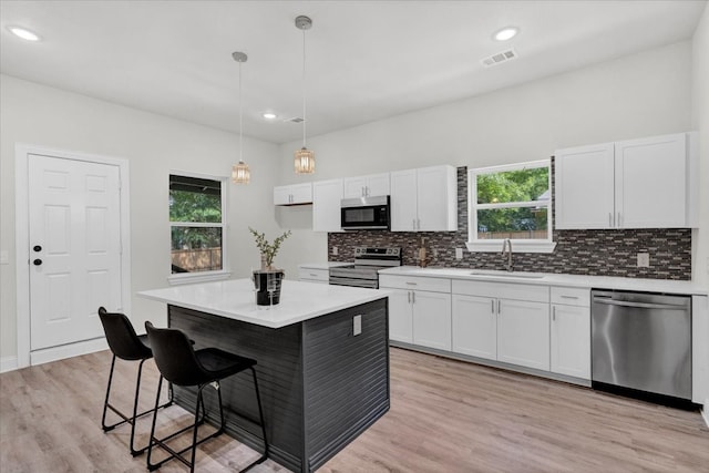 kitchen with hanging light fixtures, white cabinetry, a kitchen island, stainless steel appliances, and sink