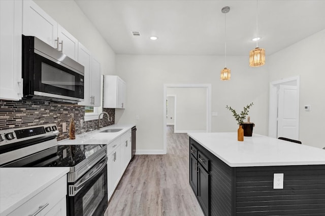 kitchen featuring appliances with stainless steel finishes, white cabinets, light wood-type flooring, decorative light fixtures, and sink