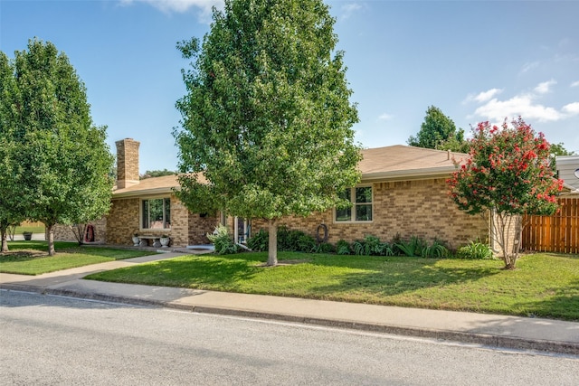 ranch-style home with a front yard, brick siding, fence, and a chimney