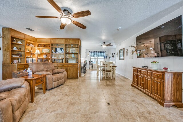 living room with ceiling fan, a brick fireplace, light tile patterned floors, and a textured ceiling