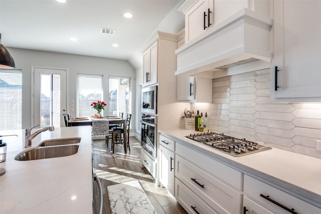 kitchen featuring custom exhaust hood, stainless steel appliances, decorative backsplash, light wood-type flooring, and sink