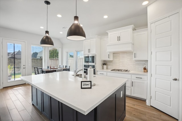 kitchen with decorative light fixtures, tasteful backsplash, a center island with sink, light hardwood / wood-style floors, and appliances with stainless steel finishes